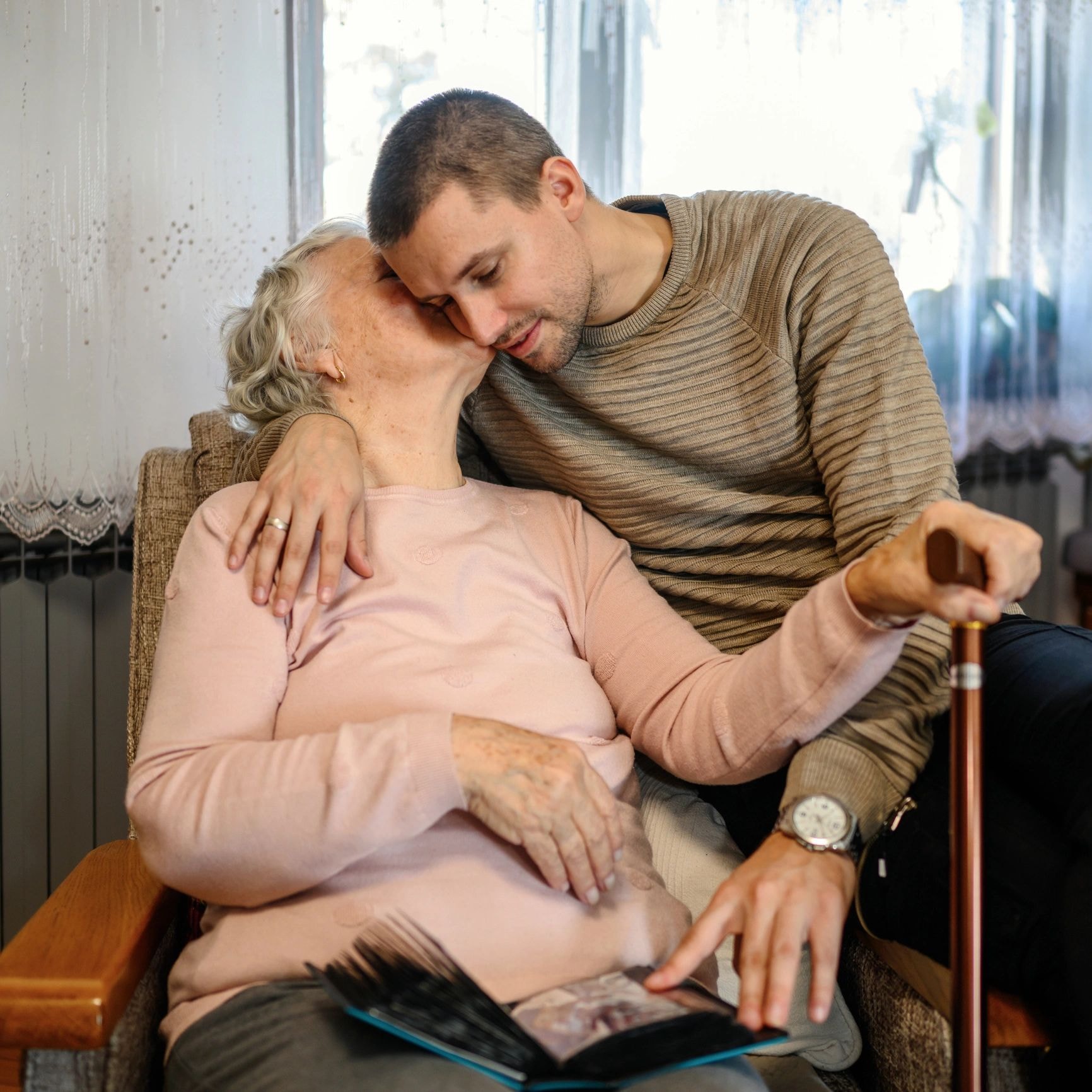 Young man and elderly woman looking at a photo album together by a window